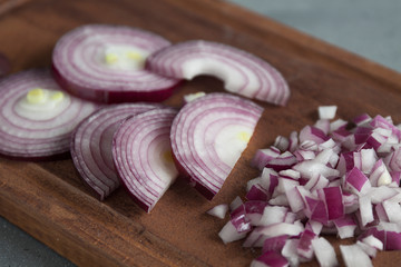 Obraz na płótnie Canvas Red onion cut into circles, half-rings and cubes on a brown wooden Board