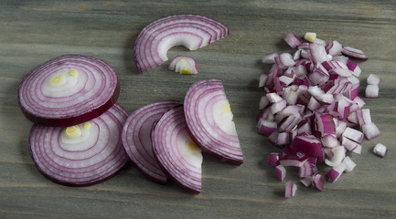 Red onions cut into circles, half-rings and cubes on a dark wooden table