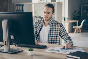 Photo of business finance administrator guy computer table look check graphics charts on paper compare with online numbers stats wear casual shirt sit modern office indoors