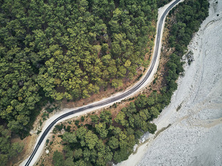 dry river bed from aerial above. Street crossing sideway with beautiful green mediterrain trees on yellow sand. white stony lake with drone in turkey