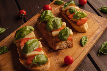 toast bread with mozzarella basil and cherry tomatoes on wooden background