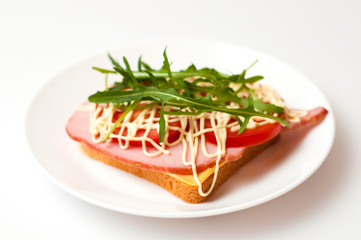 Sandwich of bread for toast, sturgeon, tomatoes, arugula, cheese and mayonnaise on a white plate in a side view