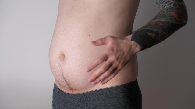 Man slams his palm on his big belly. Close up of fat man shaking his stomach. Adult play with his fat belly. Overeating. Weight loss or weight gain during quarantine. Bodypositive