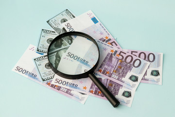 The magnifying glass is placed on 100-dollar and 500-Euro bills. Selective focus. Eurobonds