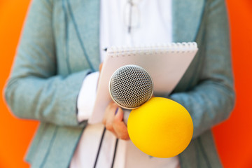 Female reporter at press conference or media event, writing notes, holding microphone. Journalism...