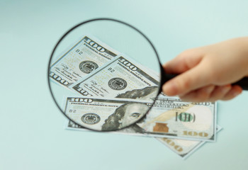 100 dollar bills under a magnifying glass. Magnifying glass in hand. Selective focus