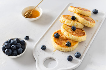 Cottage cheese pancakes with honey and blueberry on white background. Side view. Healthy breakfast recipe, restaurant menu