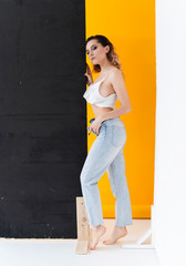 Beautiful busty girl wearing unbuttoned jeans and t-shirt poses at the black shield near yellow background. Fashionable, advertising, lifestyle and commercial design.