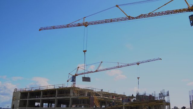 A construction crane works on a construction site against a blue sky. Construction of a covered Parking lot.