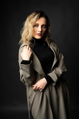 Beautiful girl wearing a casual trendy trousers, turtleneck and raincoat posing on a dark background. Fashionable, advertising, lifestyle and commercial design.