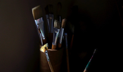 Artist's tools - paintbrushes captured in low light. The sunlight glinting off the metal ferrules...