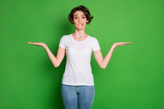 Photo Of Beautiful Lady Wavy Short Hairdo Hold Open Arms Empty Space Demonstrating Novelty Products Not Sure Which One Pick Wear Casual White T-shirt Jeans Isolated Green Color Background