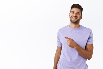 Outgoing, happy handsome hipster man pointing left, showing where get excellent tourist trip offer to have journey on holidays. Satisfied smiling man in purple t-shirt recommend promo - 339219427