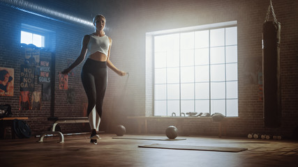 Fit Athletic Blond Woman Exercises with Jumping Rope in a Loft Style Industrial Gym. She's Concentrated on Her Intense Cross Fitness Training Program. Facility has Motivational Posters on the Wall.
