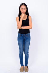 Full body shot of young beautiful Asian woman thinking