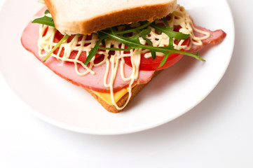 Tasty sandwich with ham or balyk, tomato, arugula, cheese, mayonnaise and white bread for toast on a plate on a white background
