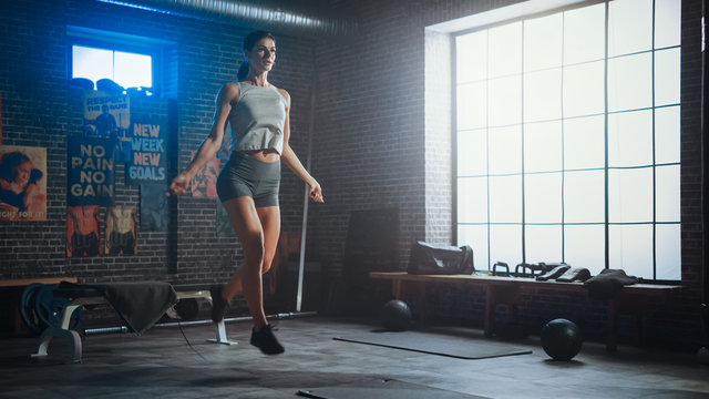 Strong Athletic Woman Exercises with Jumping Rope in a Loft Style Industrial Gym. She's Concentrated on Her Intense Cross Fitness Training Program. Facility has Motivational Posters on the Wall.