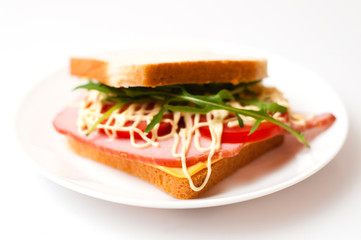 Tasty sandwich with ham or balyk, tomato, arugula, cheese, mayonnaise and white bread for toast on a plate on a white background