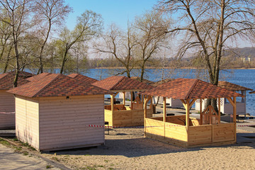 Fototapeta na wymiar Closed small wooden beach pavilions of open-air cafe in the beach near Dnipro River in Kyiv. Beautiful spring morning. Isolation period in the city. Corona virus (Covid-19) prevention. Ukraine