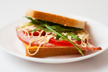 Tasty sandwich with ham or balyk, tomato, arugula, cheese, mayonnaise and white bread for toast on a plate on a white background