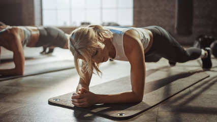 Two Young Fit Atletic Women Hold a Plank Position in Order to Exercise Their Core Strength. They are Exhausted and Struggling with Training. They Workout in a Loft Gym. - obrazy, fototapety, plakaty