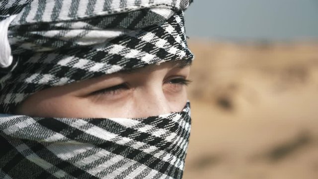 A courageous boy in keffiyeh standing in a boundless desert on a sunny day    