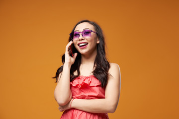 Happy girl in purple glasses talking on phone on empty orange background