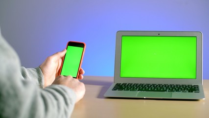 Man's hands with a smartphone on the screen of which chromakey, thumbs through the pictures. Stay home to work with a laptop with a green screen. Coronavirus or covid-19