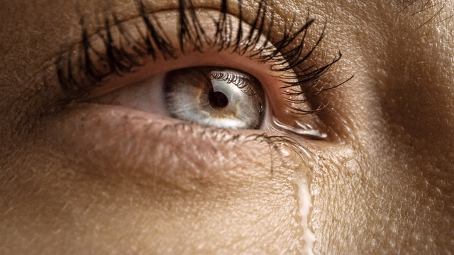 Close Up Macro Shot of a Crying Eye. Young Beatiful Female with Natural Light Blue, Yellow and Brown Color Pigmentation on the Iris. Mascara is Applied to Eyelashes. Tears are Flowing Down.