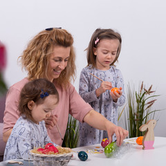 Mother and daughters are painting eggs. Happy family are preparing for Easter. Quarantine at home.