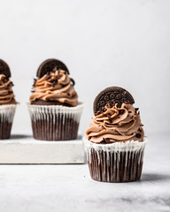 three chocolate cupcakes with cream decorated with cookies on a light background