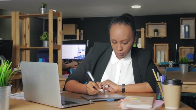 African american woman designer working at a laptop with a graphics tablet.