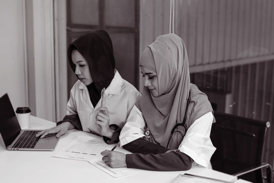 Two Female Doctors Using Laptop For Consult About Patient Treatment,with Serious Emotion,busy Time,working  At Hospital,black And White Tone,blurry Light Around