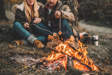 Traveler couple camping and roasting marshmallows over the fire in the forest after a hard day. Concept of trekking, adventure and seasonal vacation.