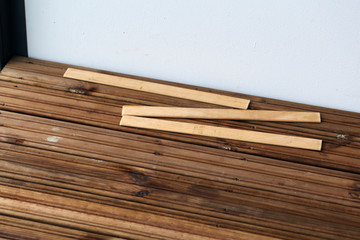 DIY building a porch / balcony floor with brown wooden planks in Espoo, Finland, spring, 2020. In this photo you can see the floor in progress and cement under it. Closeup color photo.