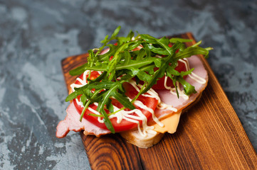 Appetizing sandwich with ham or balyk, arugula, cheese, tomatoes and mayonnaise on a cutting board...