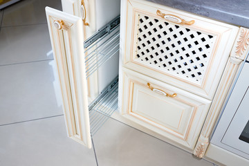 Interior of modern kitchen in classic style with golden elements in beige colors. Pull out spice rack cabinet filler pantry. Vertical drawer for spices shelf under countertop with front wooden panel.