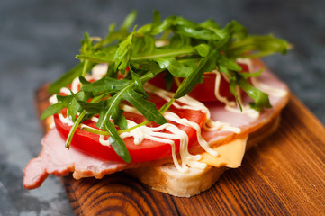 Appetizing sandwich with ham or balyk, arugula, cheese, tomatoes and mayonnaise on a cutting board side view