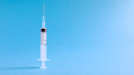 On a blue background lies a medical syringe with a needle. epidemic. Copy space The concept of collecting blood and injection vaccines, medical equipment for hypodermic injection, healthcare theme