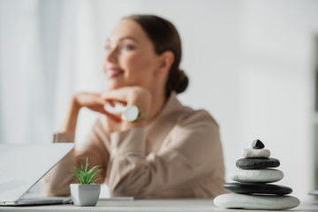 dreamy businesswoman sitting at workplace with plant, zen stones and laptop