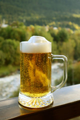 Vertical image of a pint of draft beer on the balcony railing with blurry forest view	