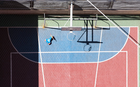 Quadra de basquete sem pessoas, vista de cima com um veloc&iacute;pede e sombra do aro projetada no ch&atilde;o.