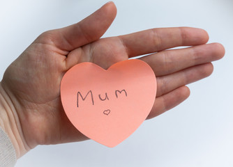 Woman's hand holding pink heart-shaped sticky note with hand written word 