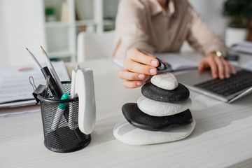 cropped view of businesswoman working with laptop at workplace with zen stones
