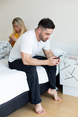 Social networks addiction and relationship problems concept. Man and woman in bed ignoring to each...