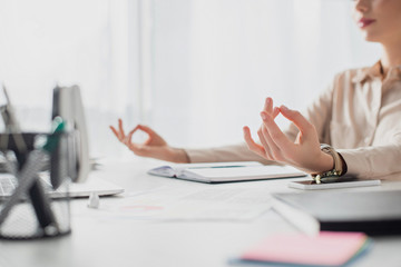 cropped view of businesswoman meditating with gyan mudra at workplace with notepad