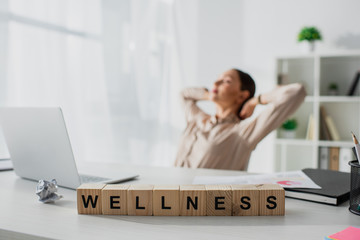 selective focus of businesswoman relaxing at workplace with laptop and alphabet cubes with wellness...