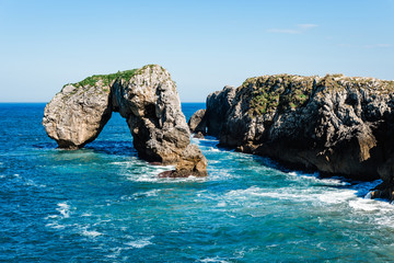 Scenic view of waves splashing against the rocky coast against blue sky. Castro de las Gaviotas...