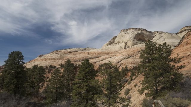A timelapse of clouds flowing over white rock faces in Zion National Park, located along the East Highway leading out of the park. Traffic passes along the road in the right of the frame.