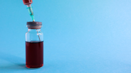 A syringe sticks out of a red liquid bottle. Isolated on a blue background. Medicine, injections,...